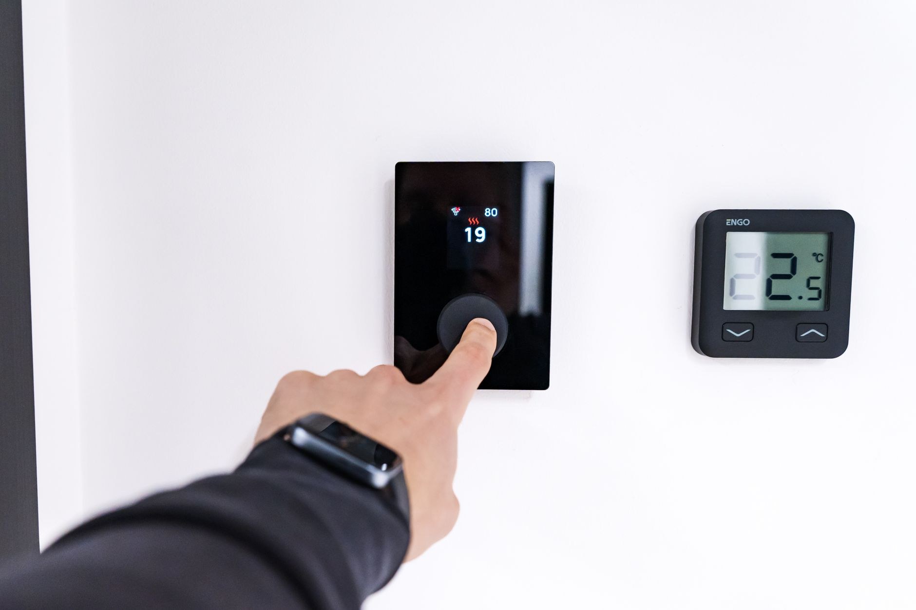 A hand setting a wall thermostat